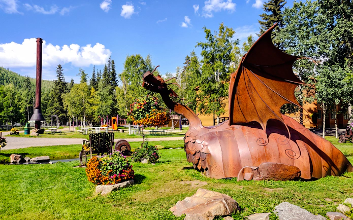 Metal dragon sculpture at Chena Hot Springs with surrounding greenery and picnic area.