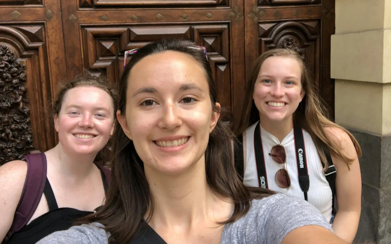 Three people smiling in front of ornate wooden doors in Turin during a self-guided city exploration game.