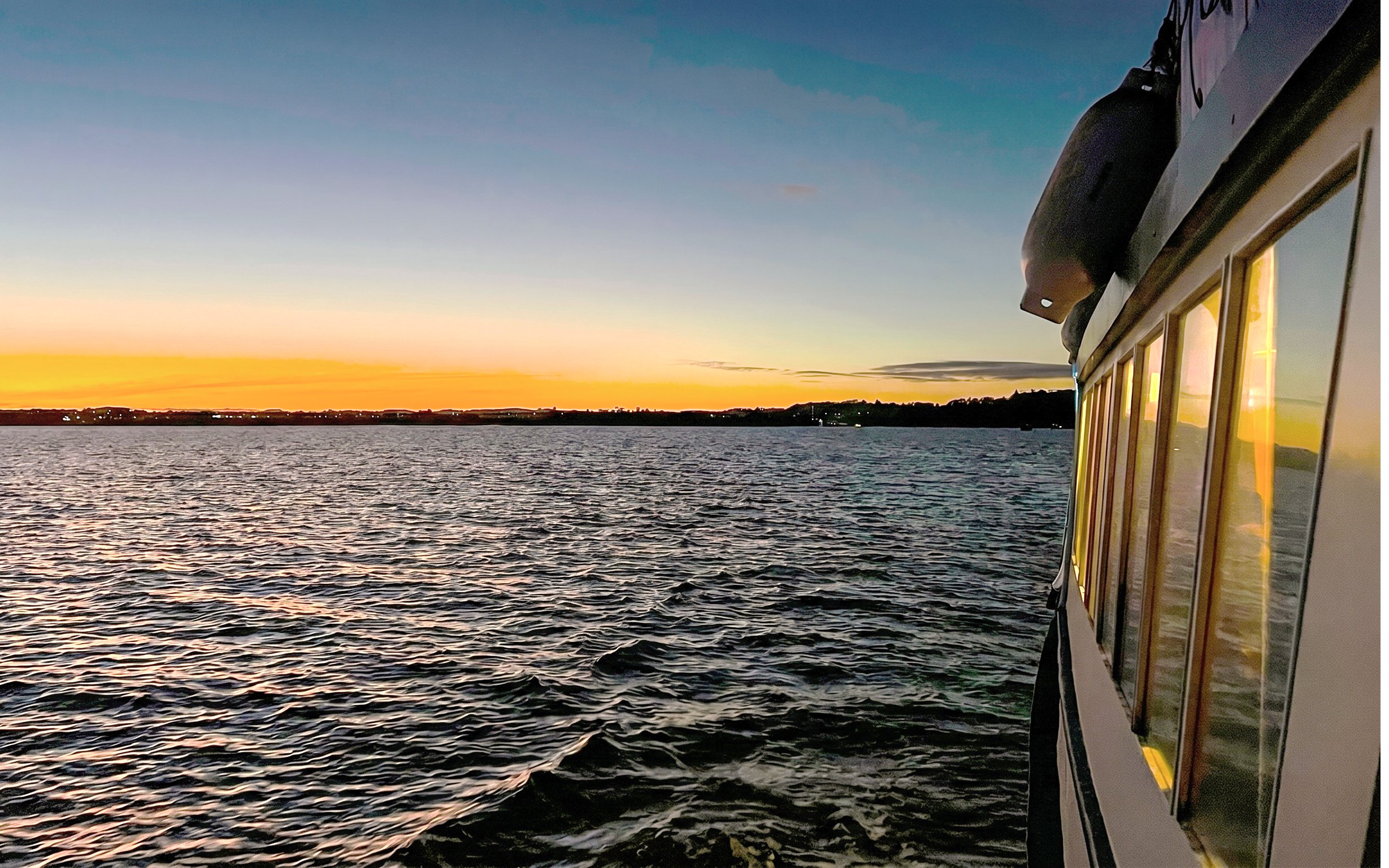 Cruise boat on Auckland Harbour at sunset with city skyline in the distance.