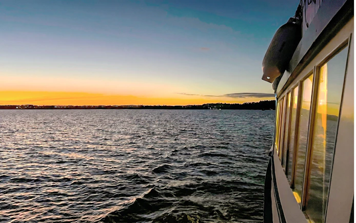 Cruise boat on Auckland Harbour at sunset with city skyline in the distance.