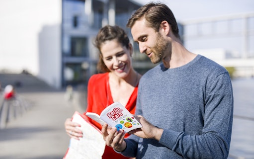 Tourists reading the Berlin Welcome Card by a city landmark.