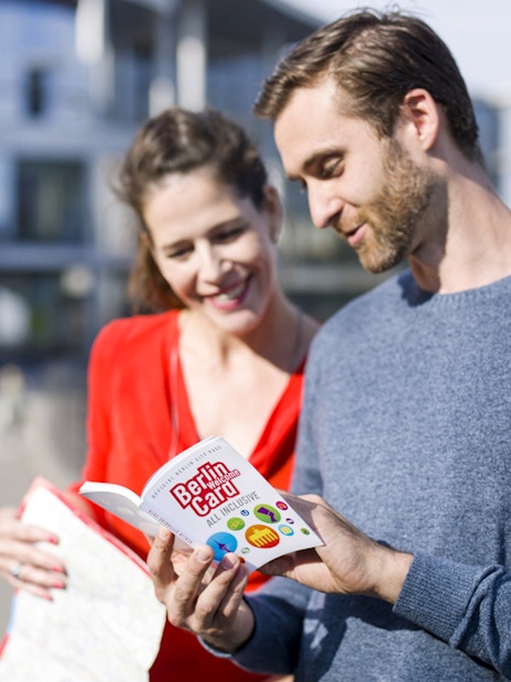 Tourists reading the Berlin Welcome Card by a city landmark.