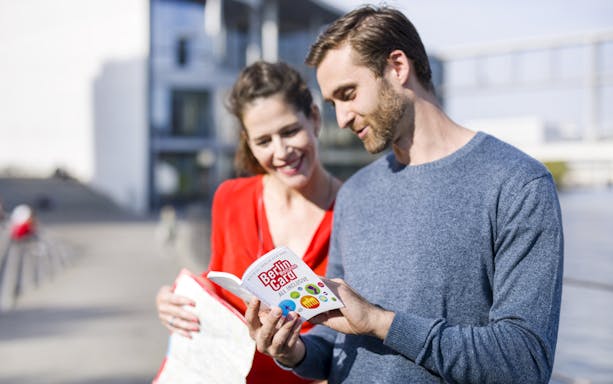 Tourists reading the Berlin Welcome Card by a city landmark.