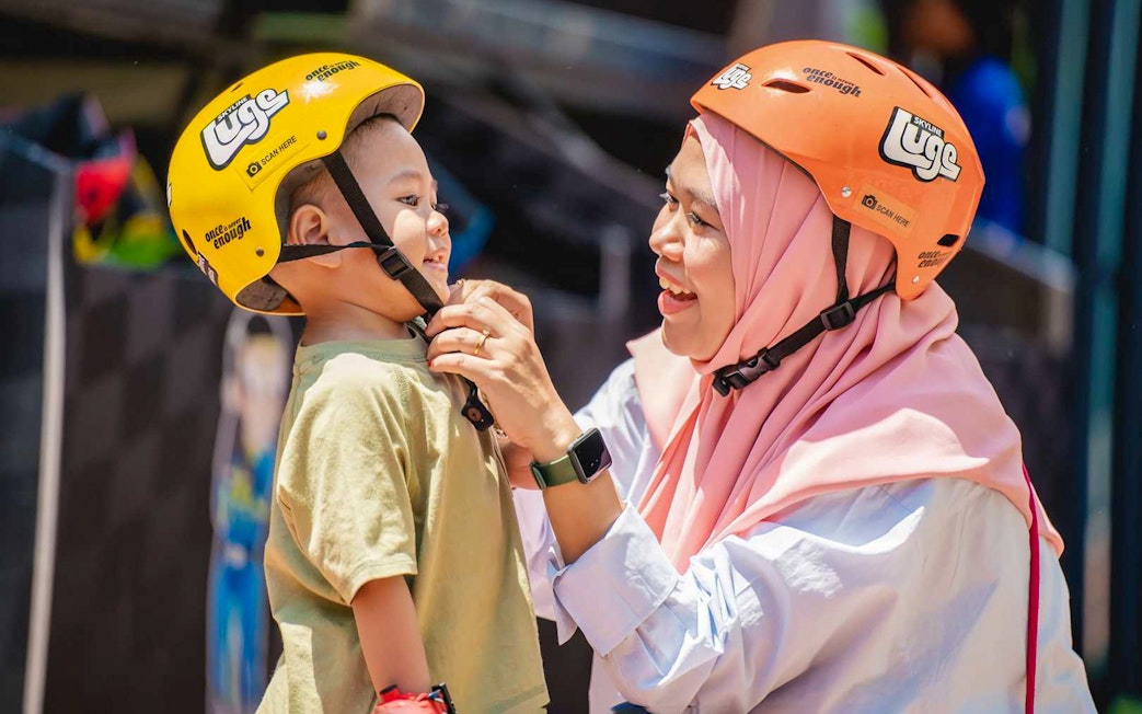 Woman adjusting child's helmet at The Skyline Luge, Kuala Lumpur.