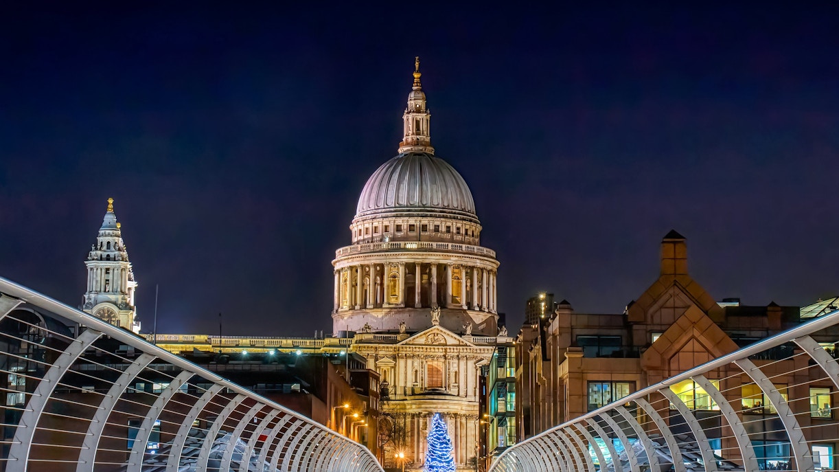 Millennium Bridge leading to St Paul's Cathedral in London at night with Christmas lights.