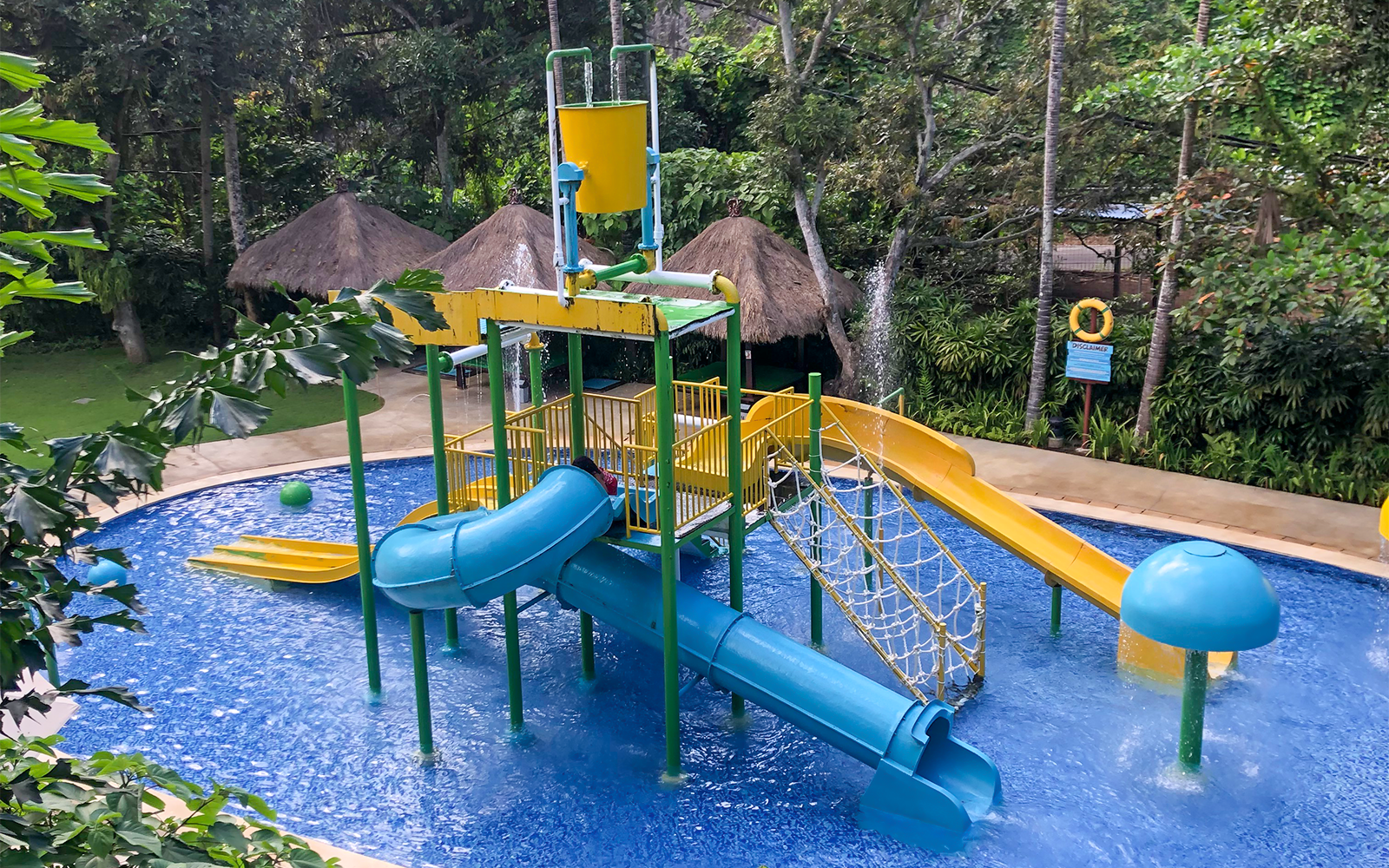 Water play area with slides and splash bucket at Bali Zoo jungle setting.