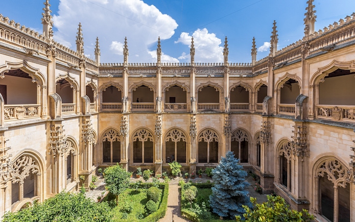 Cloisters of San Juan de Los Reyes Monastery with ornate arches and lush garden.