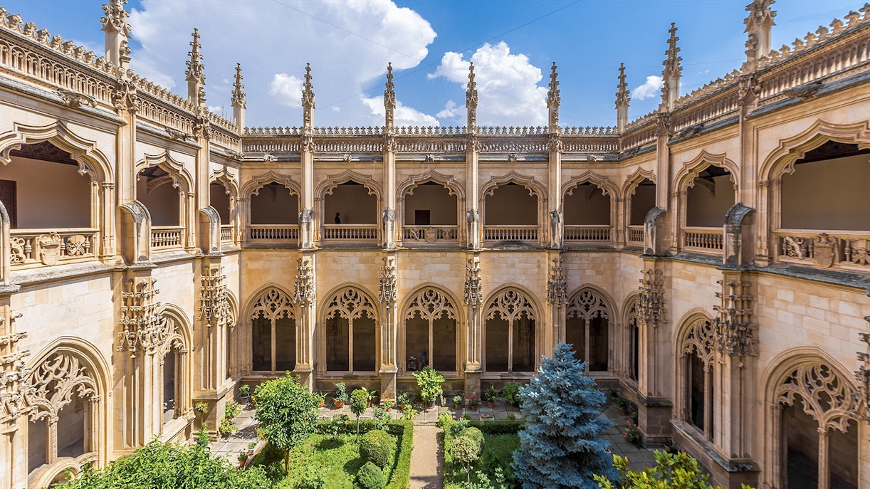 Cloisters of San Juan de Los Reyes Monastery with ornate arches and lush garden.