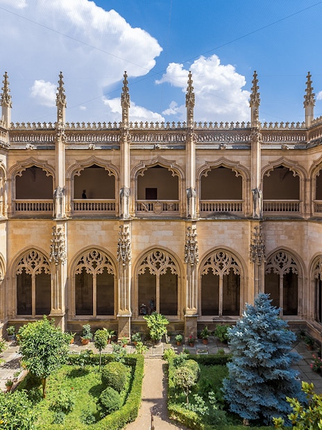 Cloisters of San Juan de Los Reyes Monastery with ornate arches and lush garden.