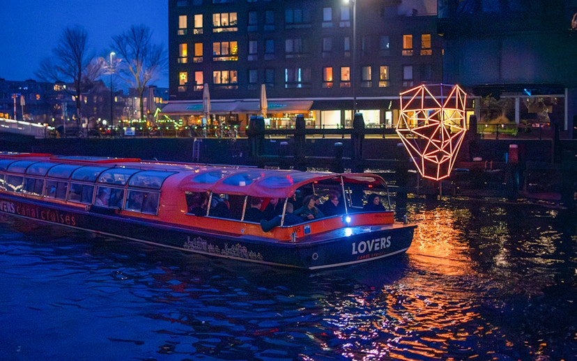 Amsterdam canal boat with passengers on a dinner cruise at night, illuminated by city lights.
