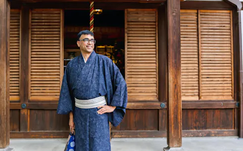 Man in traditional kimono standing in front of wooden building in Kyoto.