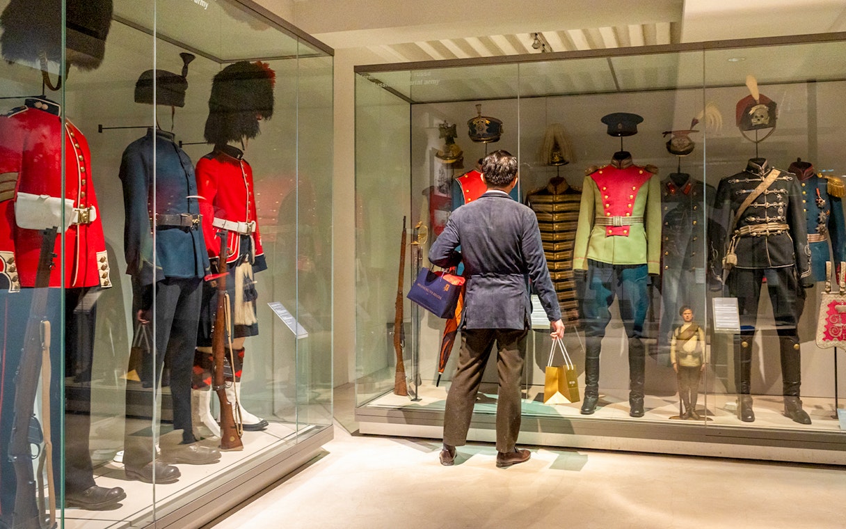 Army uniforms on display at The Army Museum with visitor observing.