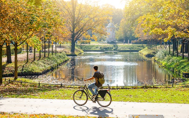 Cyclist in park during guided bike tour, autumn trees and pond in background.