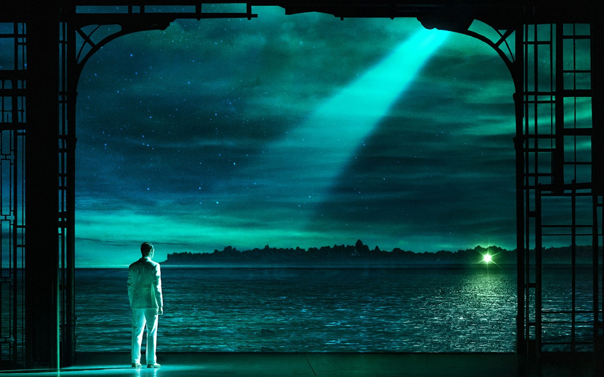 Man in white suit gazing at green light across water, scene from The Great Gatsby.