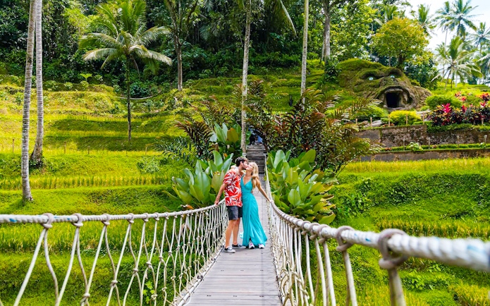 Couple kissing on a suspension bridge at Alas Harum, Bali, surrounded by lush greenery.
