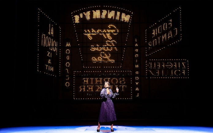 Performer on stage with illuminated theater signs in the background during a "Gypsy" show.