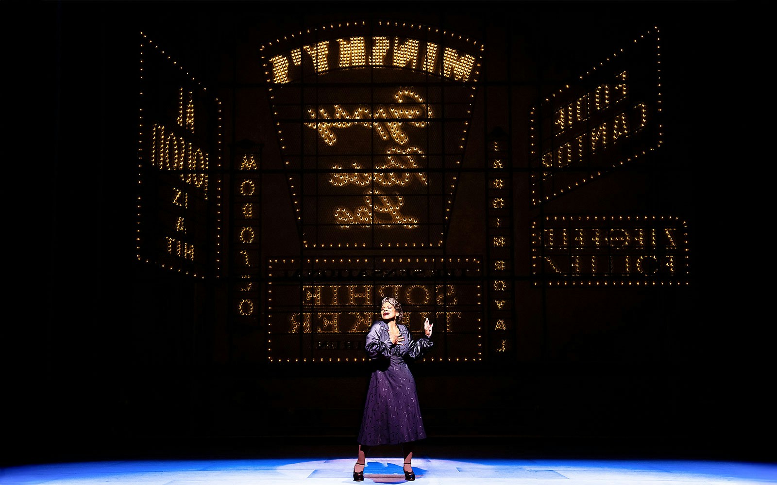 Performer on stage with illuminated theater signs in the background during a "Gypsy" show.