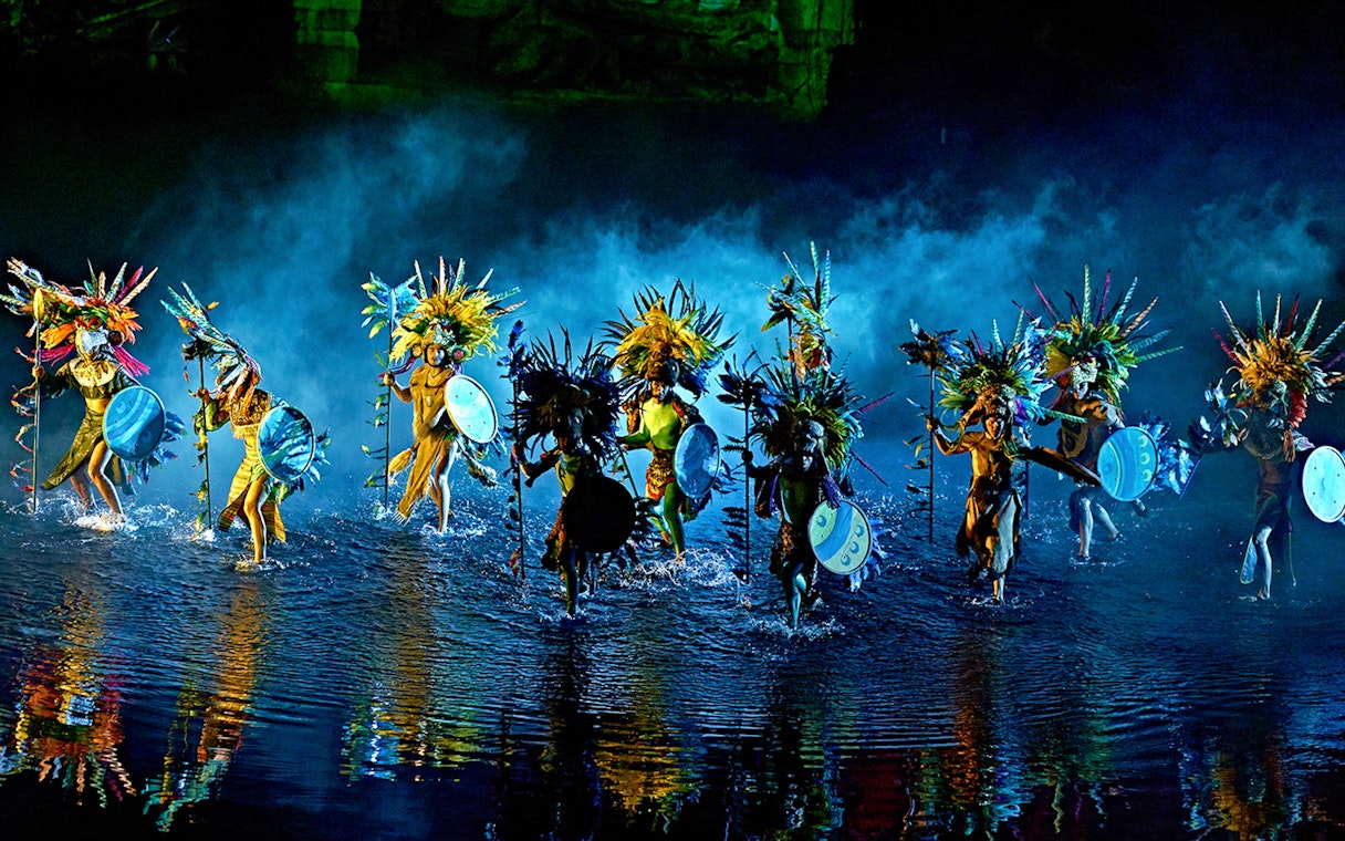 Performers in colorful costumes with shields and headdresses in "The Dream of Toledo" show.