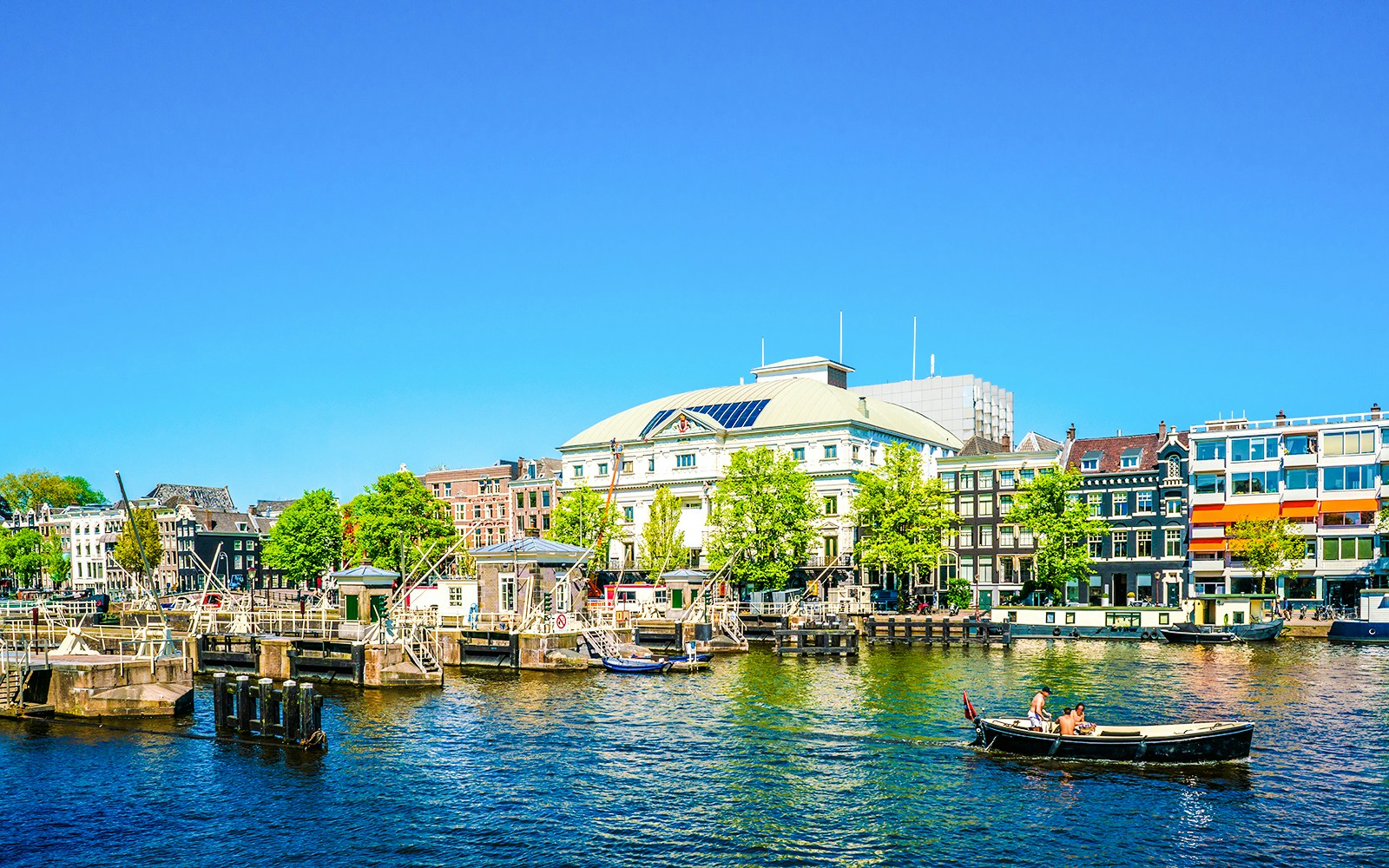 Royal Theater Carré by the Amstel River in Amsterdam with boats and historic buildings nearby.