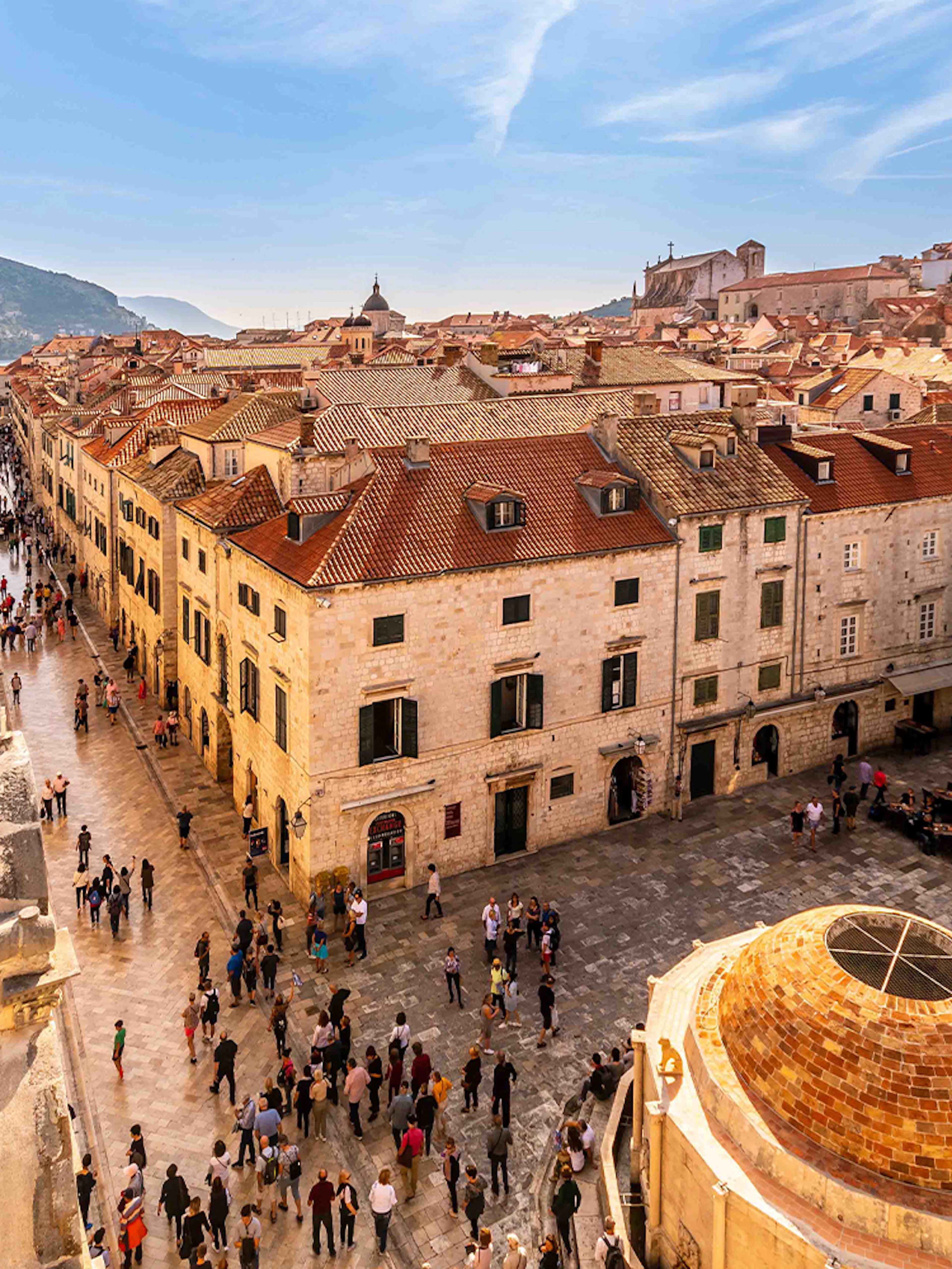 Dubrovnik Old Town street with people walking near historic buildings and bell tower.