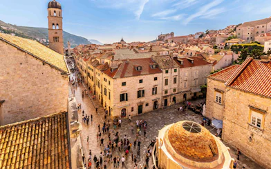 Dubrovnik Old Town street with people walking near historic buildings and bell tower.