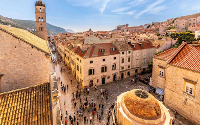 Dubrovnik Old Town street with people walking near historic buildings and bell tower.