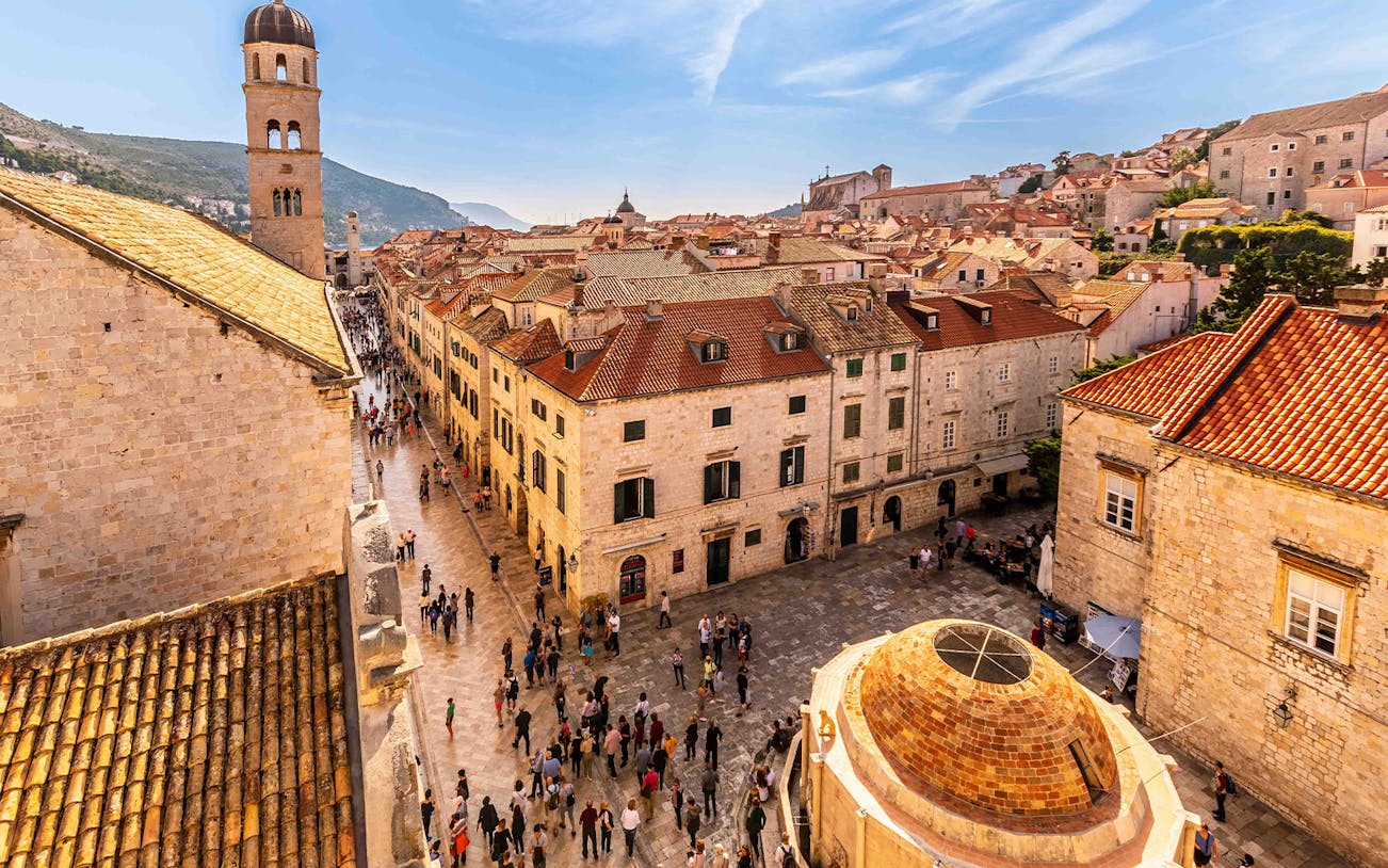 Dubrovnik Old Town street with people walking near historic buildings and bell tower.