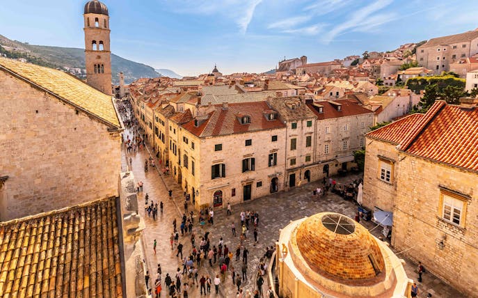 Dubrovnik Old Town street with people walking near historic buildings and bell tower.