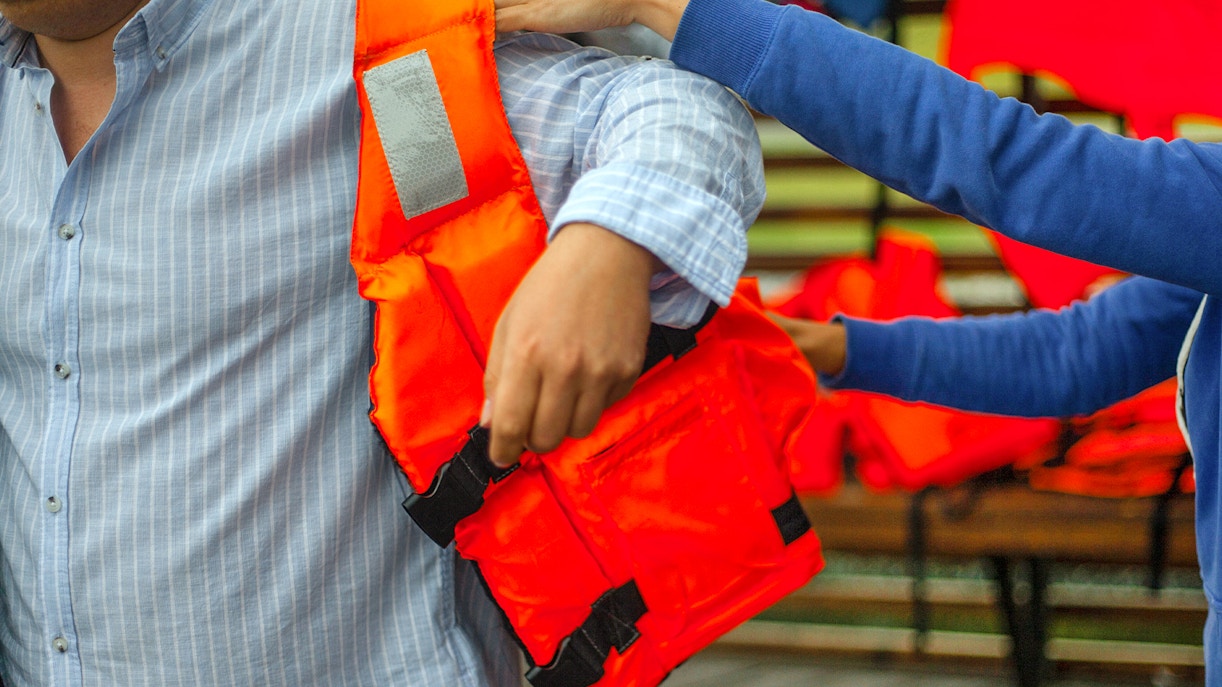 Person assisting another with a life jacket before a water activity.