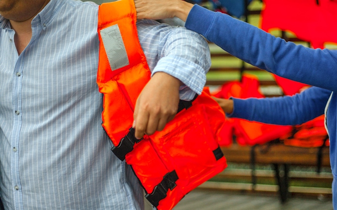 Person assisting another with a life jacket before a water activity.