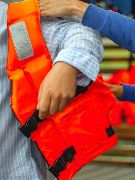 Person assisting another with a life jacket before a water activity.