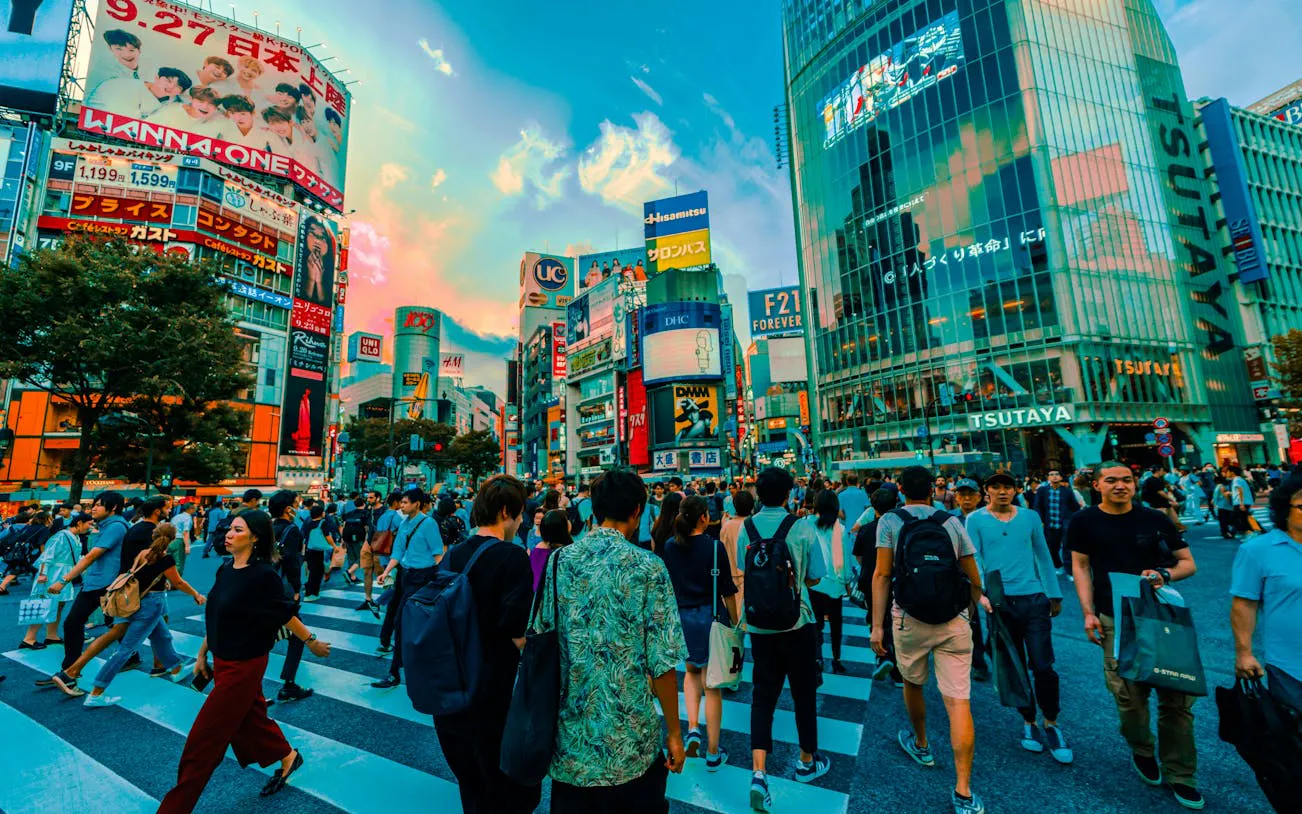 Crowds crossing Shibuya Crossing in Tokyo with colorful billboards and cityscape.