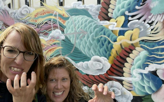 Colorful dragon mural in San Francisco Chinatown with two people posing playfully in front.