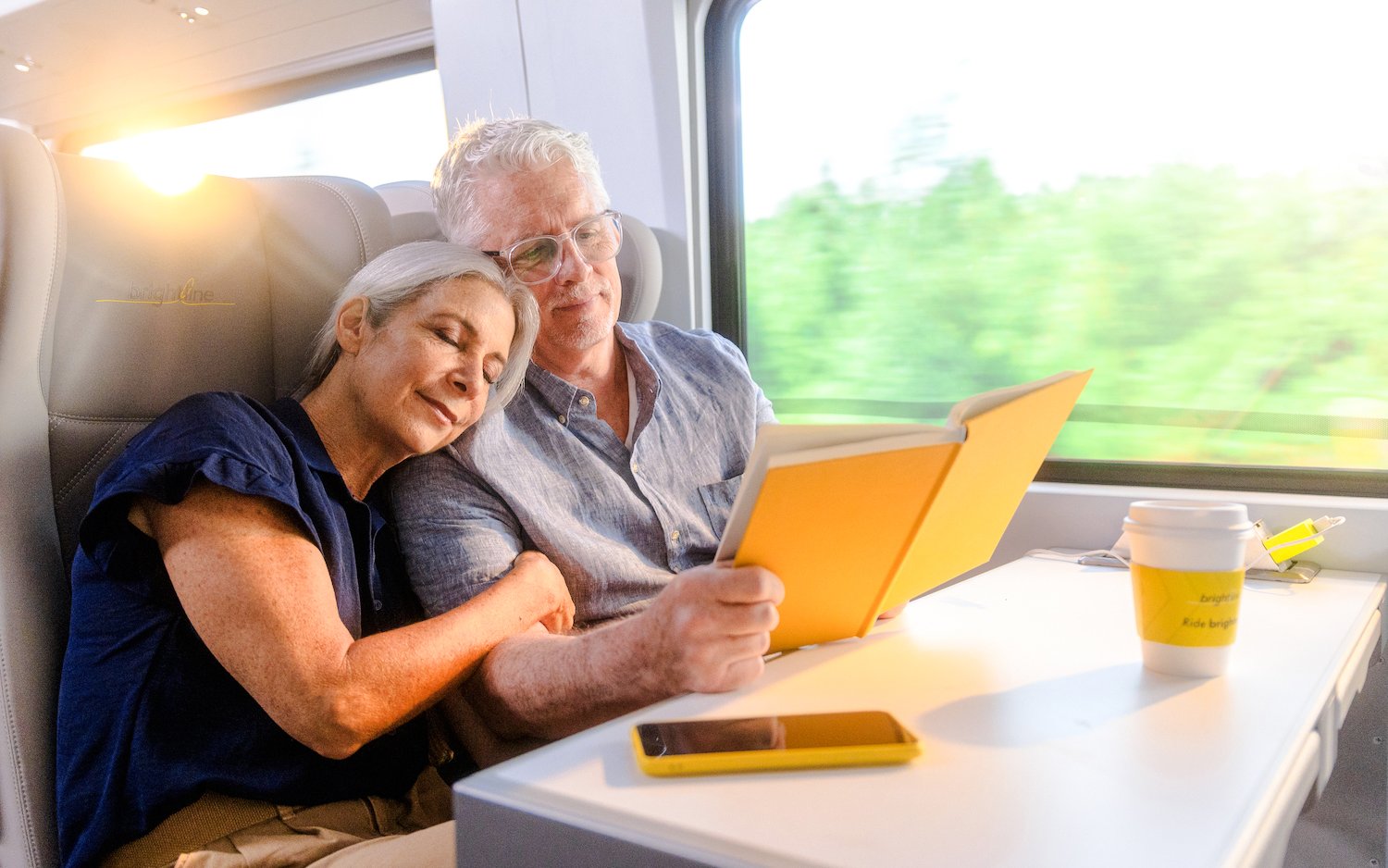 Couple relaxing on Brightline train from Miami to Orlando, reading and enjoying the journey.