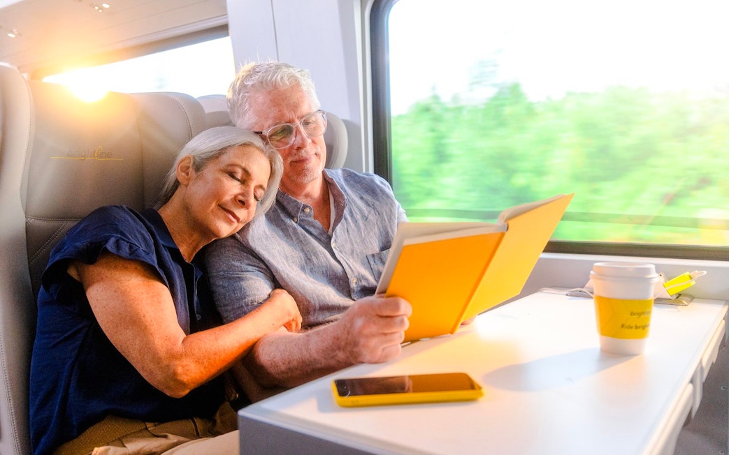 Couple relaxing on Brightline train from Miami to Orlando, reading and enjoying the journey.