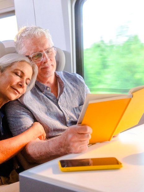 Couple relaxing on Brightline train from Miami to Orlando, reading and enjoying the journey.