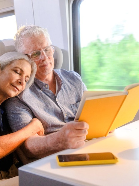 Couple relaxing on Brightline train from Miami to Orlando, reading and enjoying the journey.