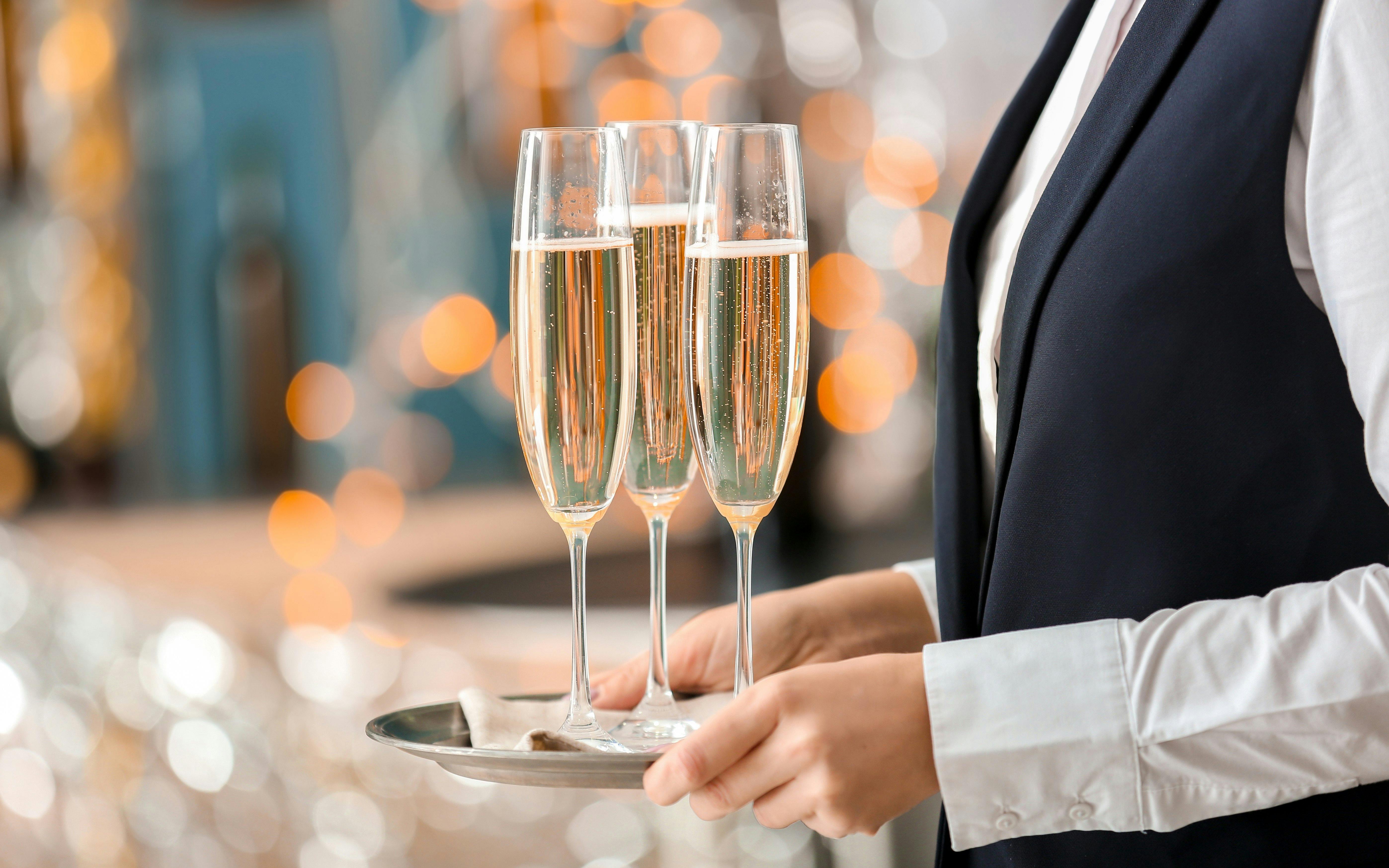 Server holding a tray with three champagne flutes during table service.