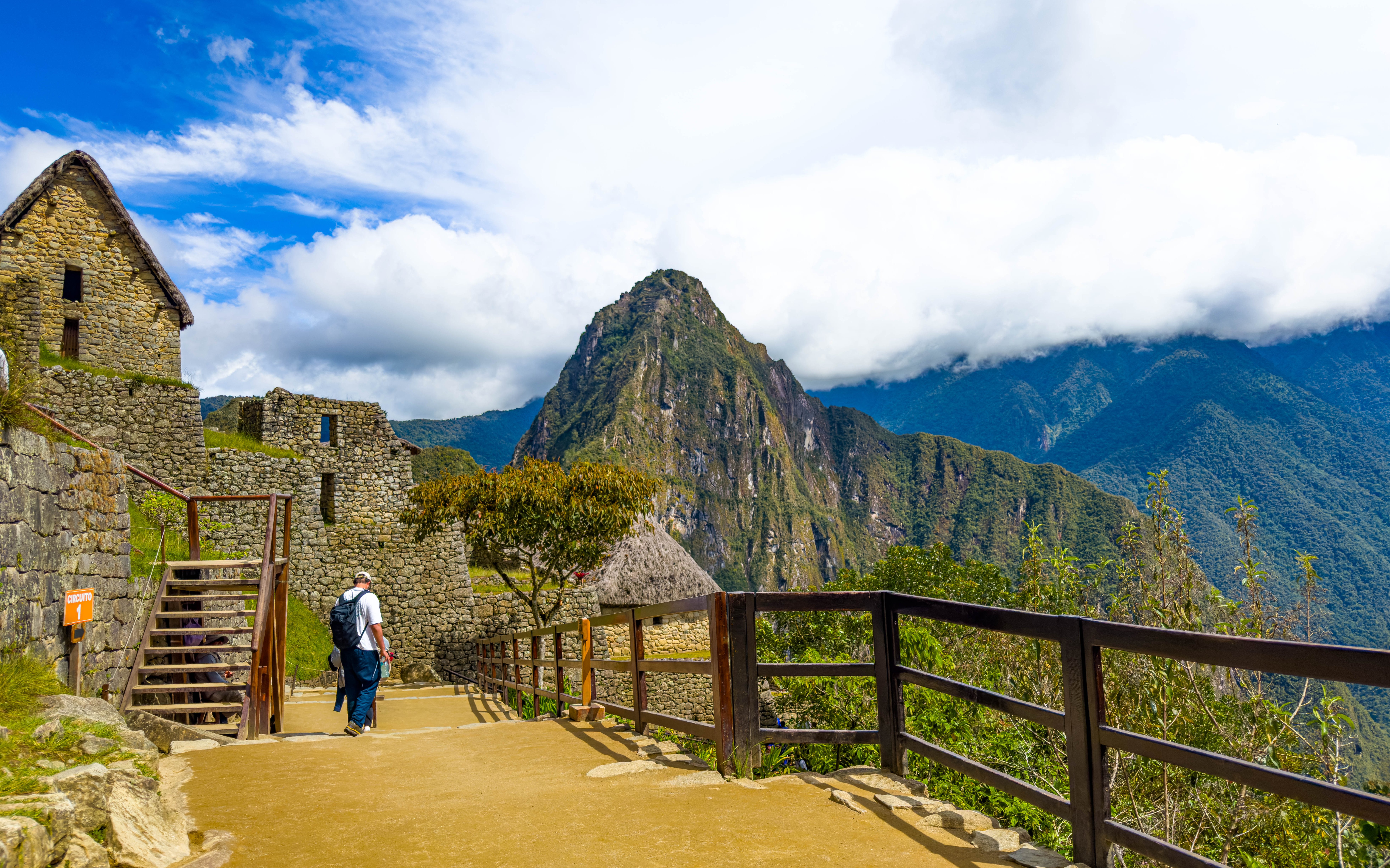 Visitor walking along stone path at Machu Picchu with Huayna Picchu in the background, Peru.