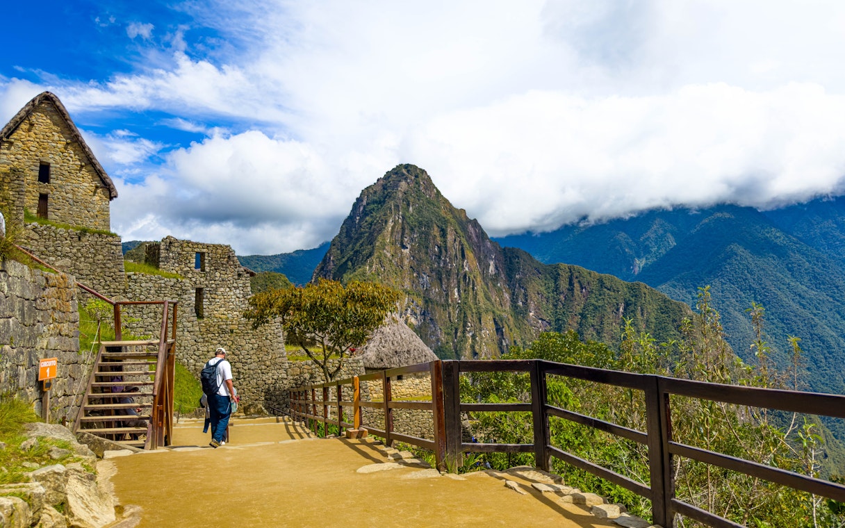Visitor walking along stone path at Machu Picchu with Huayna Picchu in the background, Peru.