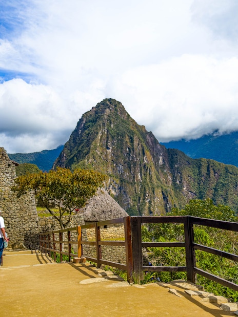 Visitor walking along stone path at Machu Picchu with Huayna Picchu in the background, Peru.