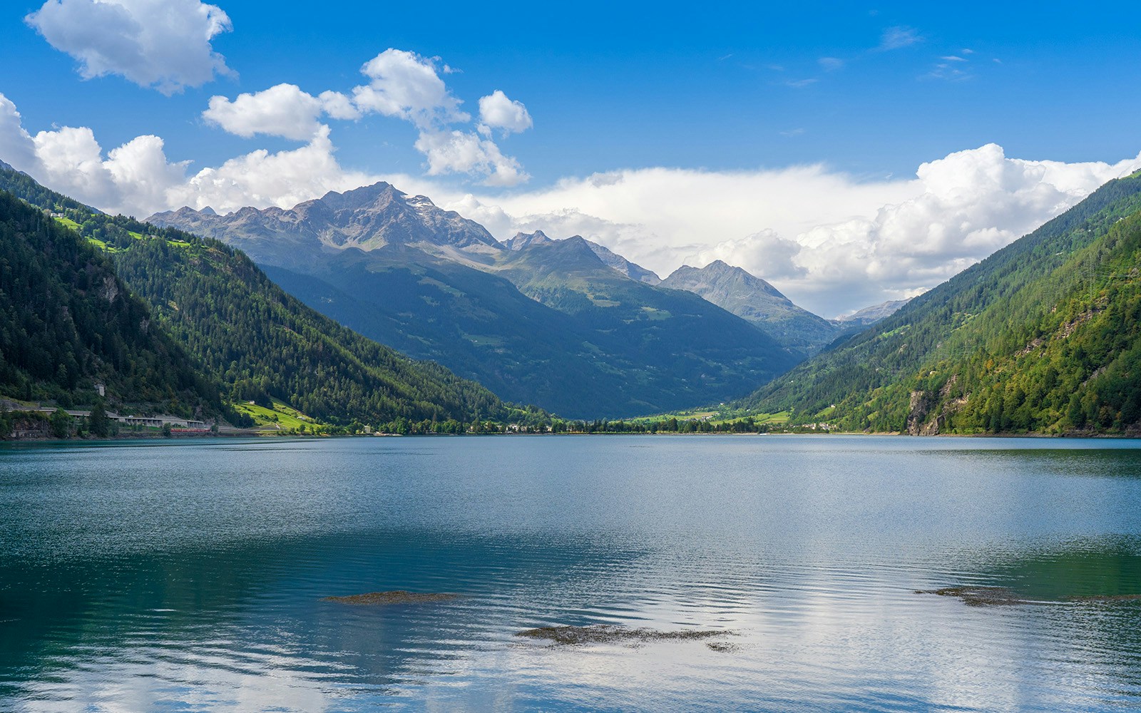 Swiss alpine lake in the mountains, Poschiavo (Miralago), Switzerland. Bernina massive peaks in the background of the green valley, blue sky with clouds