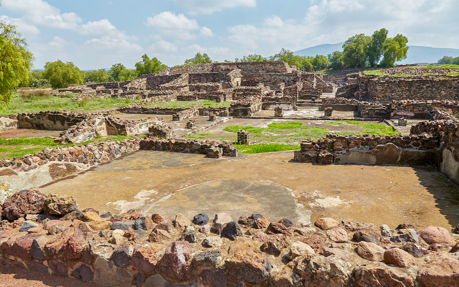 Ruins of Teotihuacan with ancient stone structures and greenery in the background.