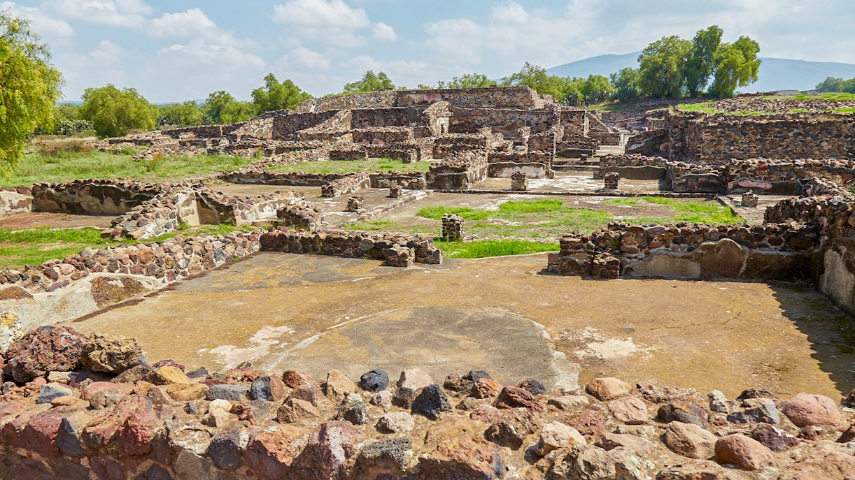 Ruins of Teotihuacan with ancient stone structures and greenery in the background.
