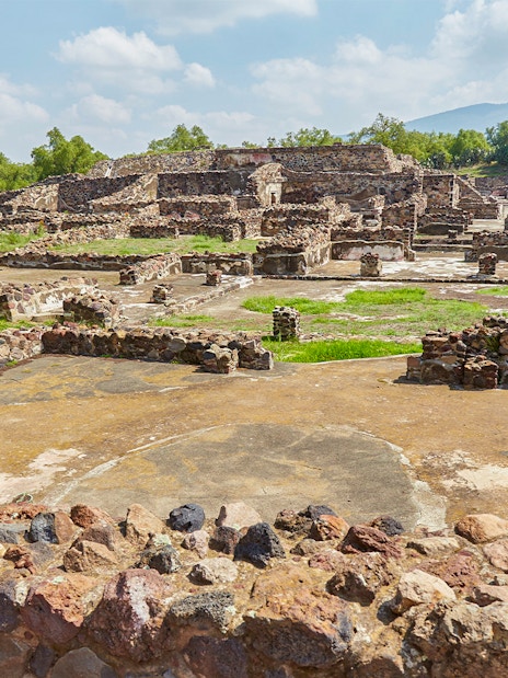Ruins of Teotihuacan with ancient stone structures and greenery in the background.