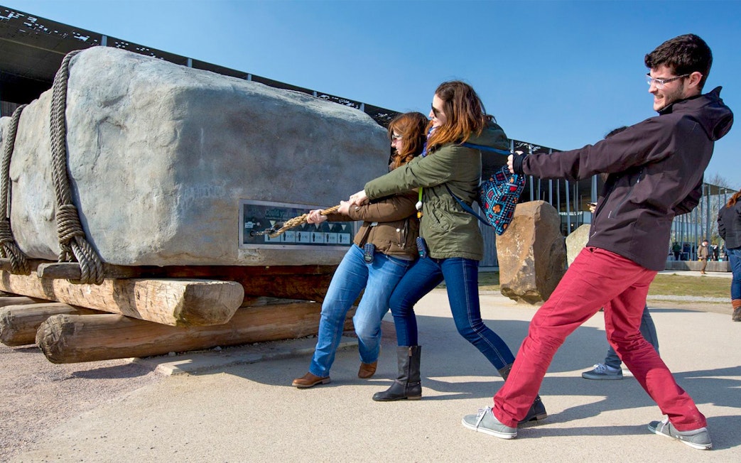 Visitors pulling a large stone replica at Stonehenge exhibit during half-day tour from London.