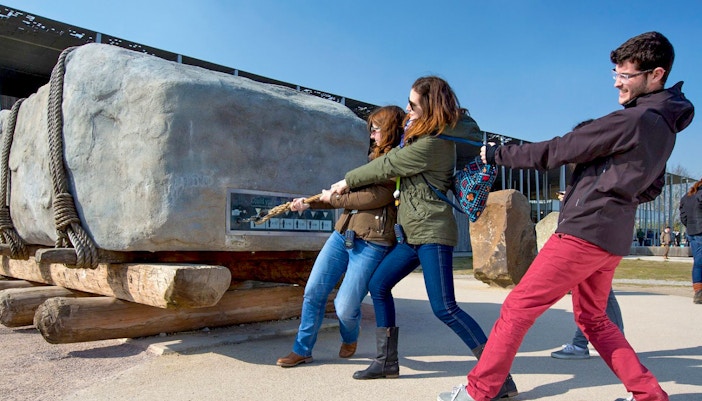 Visitors pulling a large stone replica at Stonehenge exhibit during half-day tour from London.