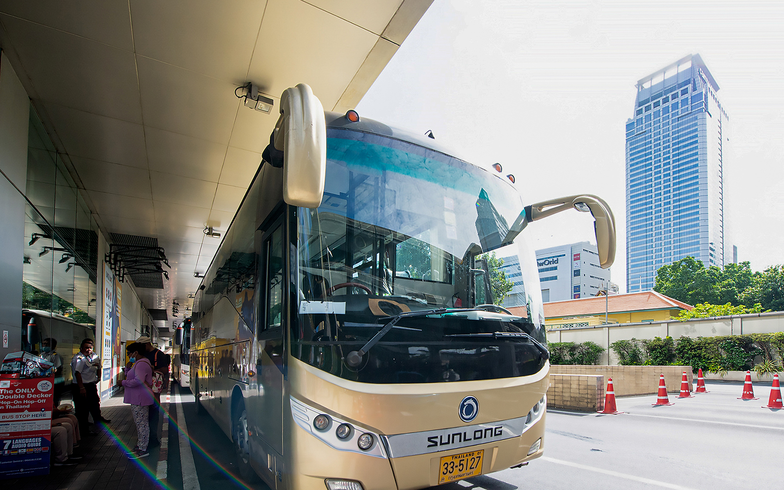 Tour bus parked at a station in Bangkok, Thailand, with passengers boarding.