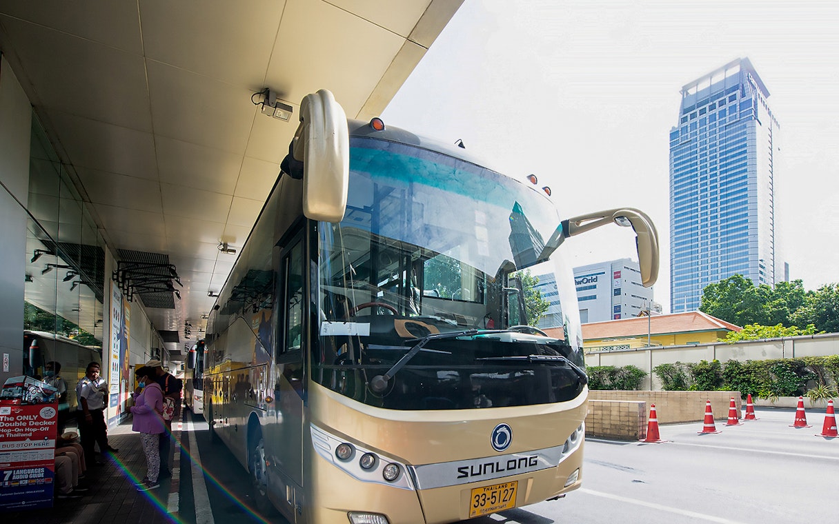 Tour bus parked at a station in Bangkok, Thailand, with passengers boarding.