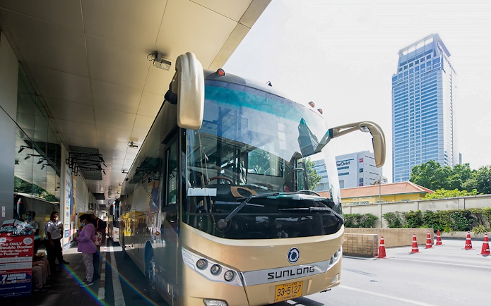 Tour bus parked at a station in Bangkok, Thailand, with passengers boarding.
